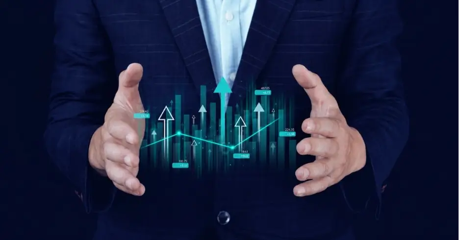 A close-up of a person wearing a dark pinstripe suit jacket over a light-colored dress shirt, holding their hands open as if framing a digital graphic. Floating between their hands is a glowing teal and blue financial bar graph featuring upward-pointing arrows, a connecting trend line, and small digital data labels against a dark background.