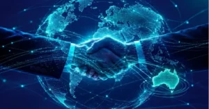 A digital, neon-blue illustration of two business suits shaking hands in front of a glowing, holographic globe covered in network connection lines, with a highlighted map of Australia visible in the foreground.