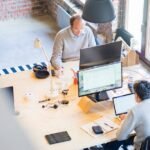 Banner reading “Enhancing Scalability and Agility Through Financial Outsourcing” with two professionals collaborating at a desk with laptops and monitors in a modern office.